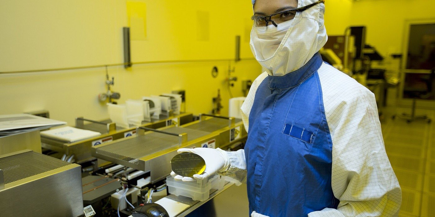 Researcher in cleanroom coveralls holding a finished silicon wafer